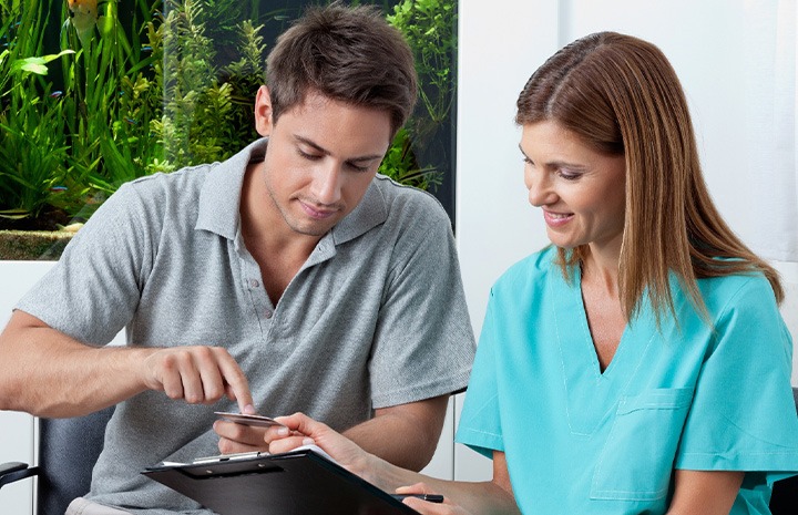 Woman in teal scrubs aking credit card information from patient for paperwork