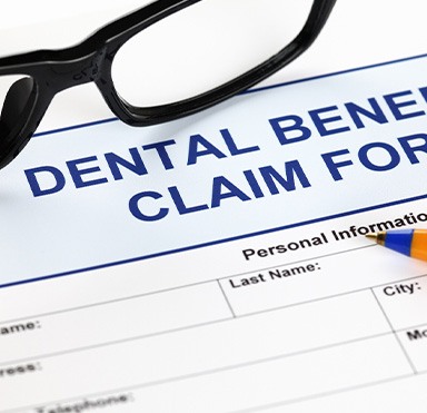 Black-framed glasses at top of blue dental benefits claim form
