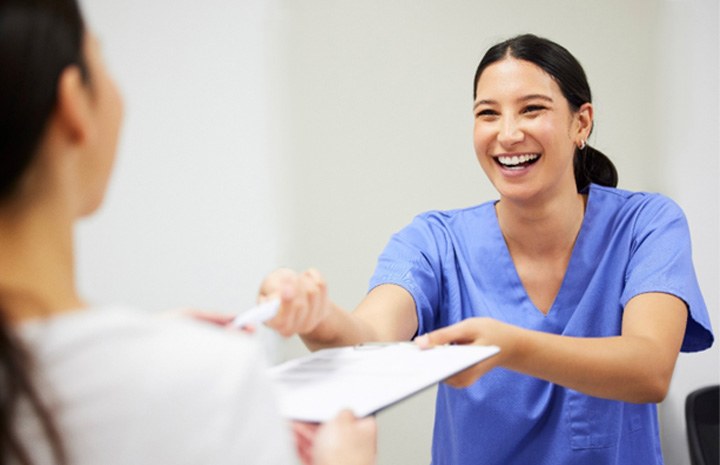 Dental assistant smiling while handing patient form