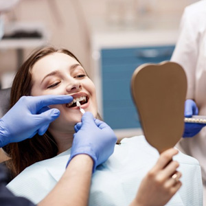 Patient smiling as dentist compares a veneer to her tooth