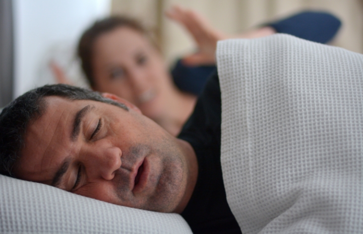 Woman frustrated in bed next to snoring man